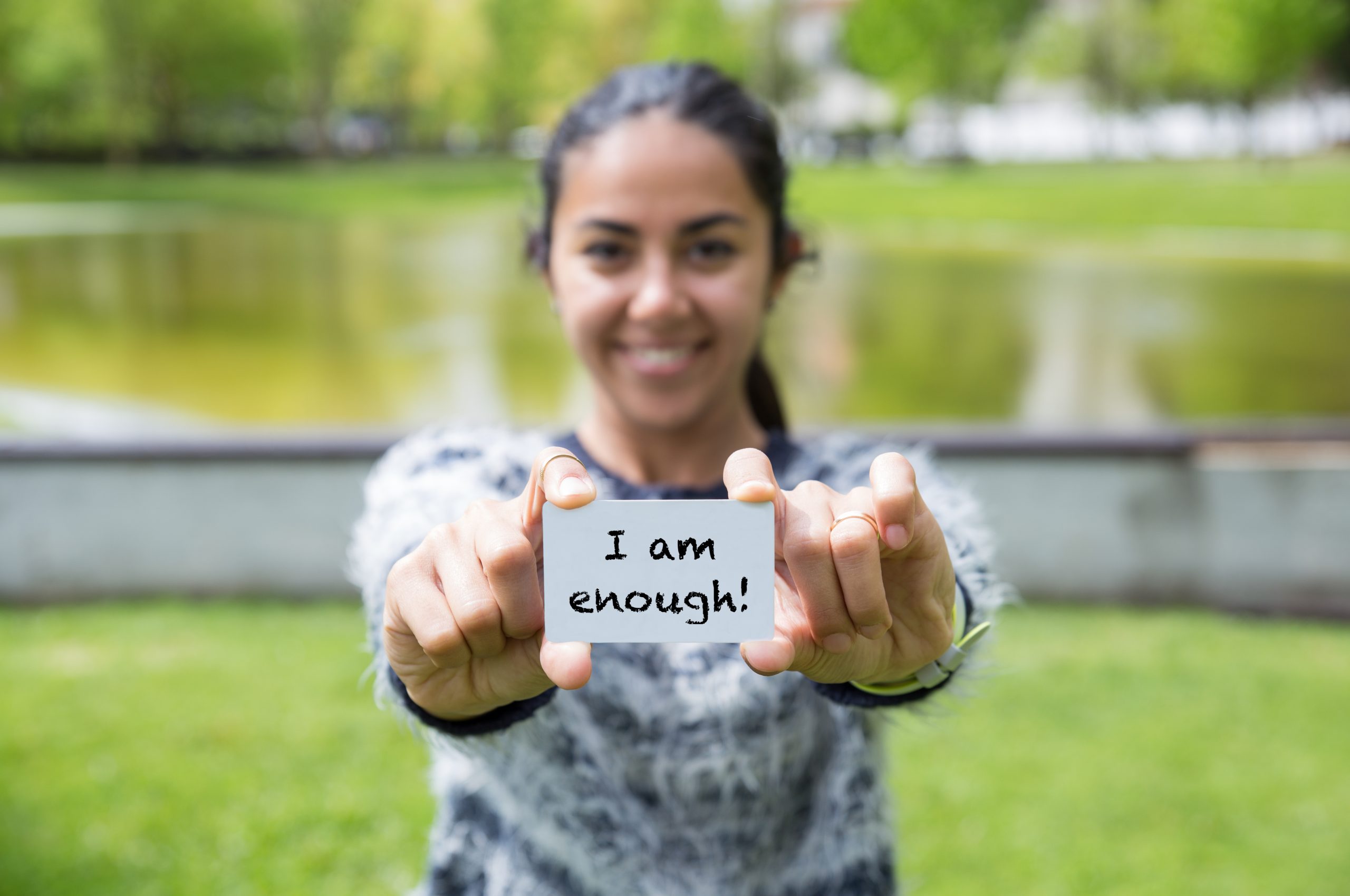 Smiling young woman showing "I am enough" at the park